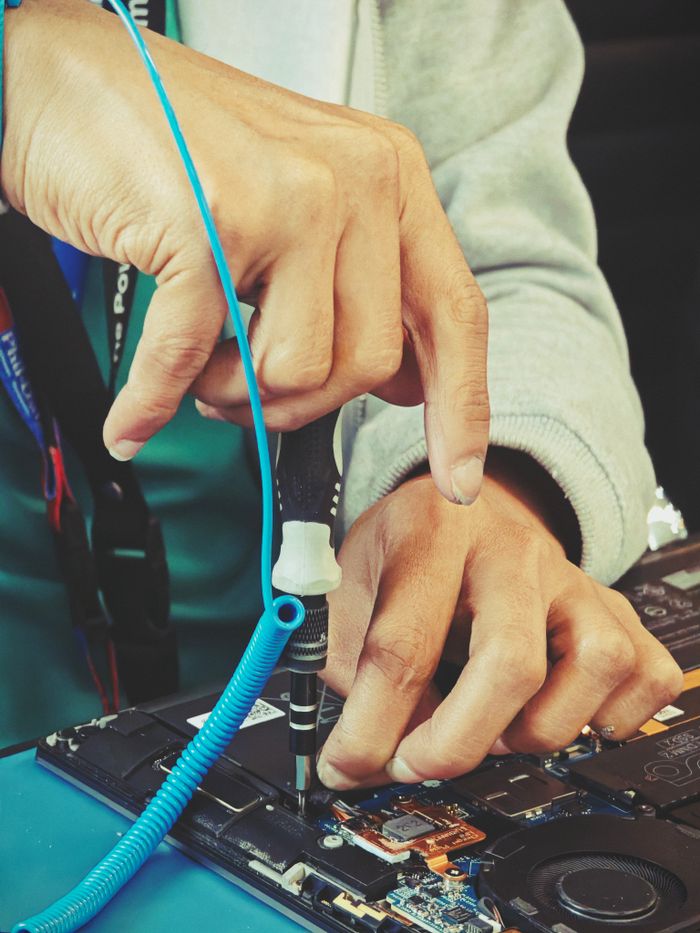 About Close-up of a technician's hands repairing a laptop's internal components with tools.